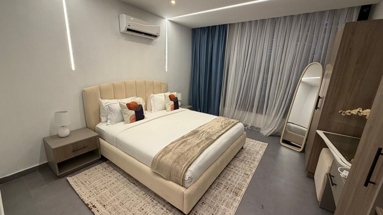 Ein modernes Hotelzimmer mit einem großen Bett, Nachttischen, einem Kleiderschrank und einer Klimaanlage.