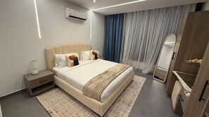 A modern hotel room with a large bed, bedside tables, a wardrobe, and an air conditioning unit. - Cozy 1 bedroom Studio Apartment with Pool in Gombe (Kinshasa)