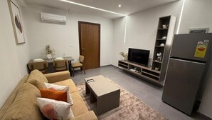 A modern living room with a sofa, coffee table, TV, and built-in shelving. - Cozy 1 bedroom Studio Apartment with Pool in Gombe (Kinshasa)