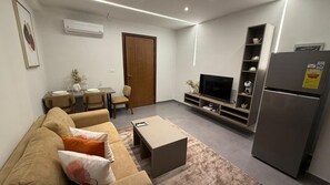 A modern living room with a sofa, coffee table, TV, and built-in shelving. - Cozy 1 bedroom Studio Apartment with Pool in Gombe (Kinshasa)
