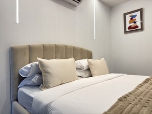 A neatly made bed with a beige headboard, white bedding, and a few pillows.