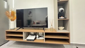 Un salon moderne avec un téléviseur à écran plat posé sur un meuble télé en bois, un vase contenant des fleurs séchées et une petite étagère ornée d’objets décoratifs.