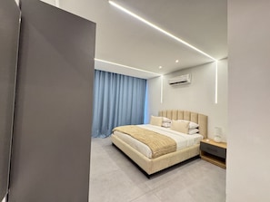 A modern bedroom with a large bed, bedside tables, and an air conditioning unit. - 1 bdrm Studio Apartment with Pool, gym, restaurant (Kinshasa)