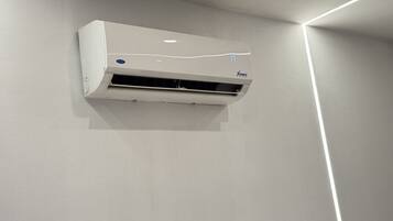 A white air conditioning unit mounted on a plain wall with a modern light fixture.