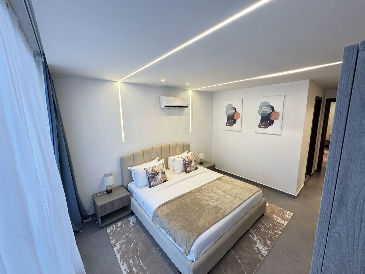 Een moderne hotelkamer met een bed, nachtkastje, lamp en kunstwerk aan de muur.
