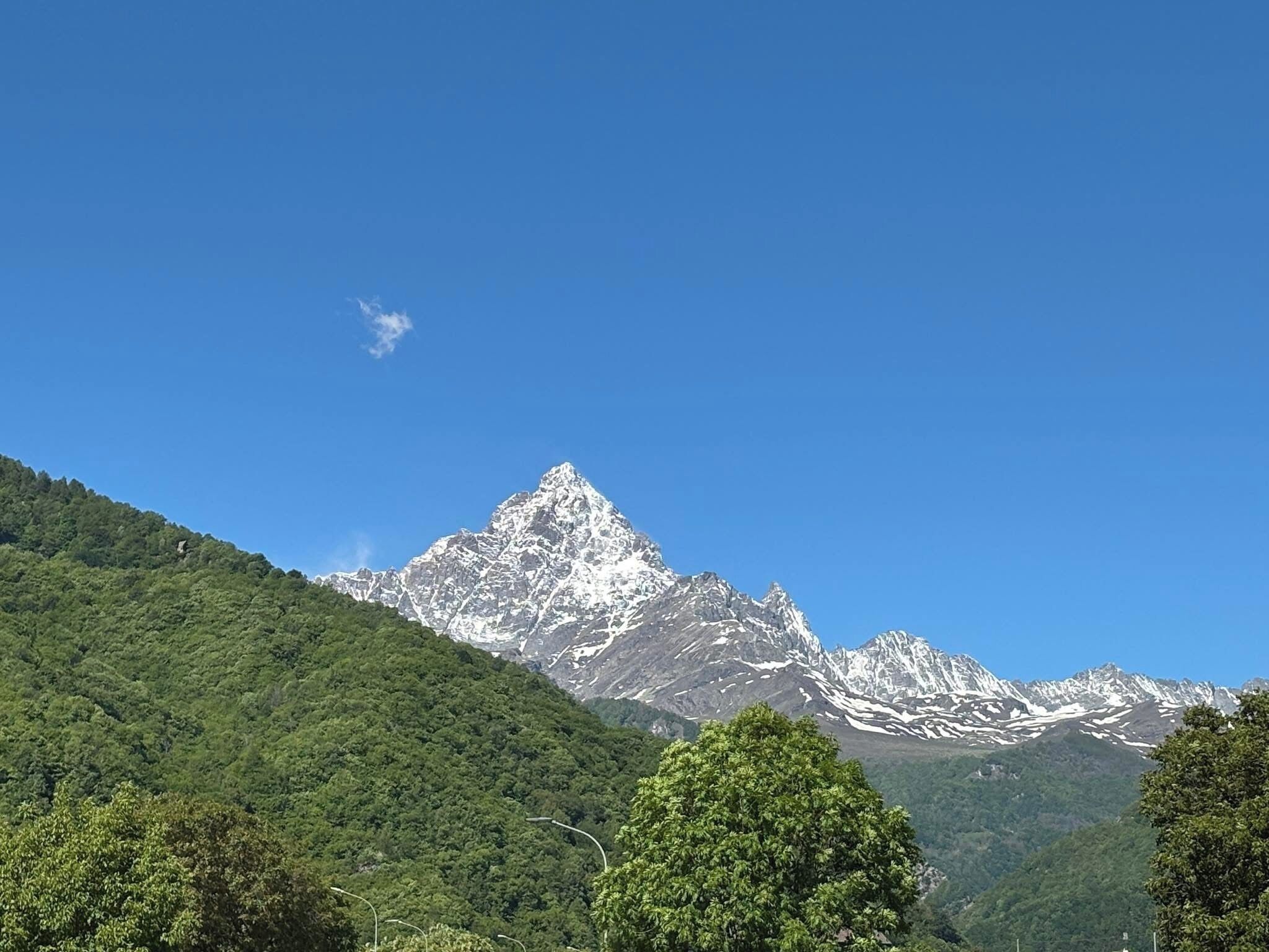 Eine Bergkette mit einem markanten Gipfel, üppig grünen bewaldeten Hängen und blauem Himmel.