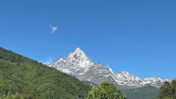 Eine Bergkette mit einem markanten Gipfel, üppig grünen bewaldeten Hängen und blauem Himmel.