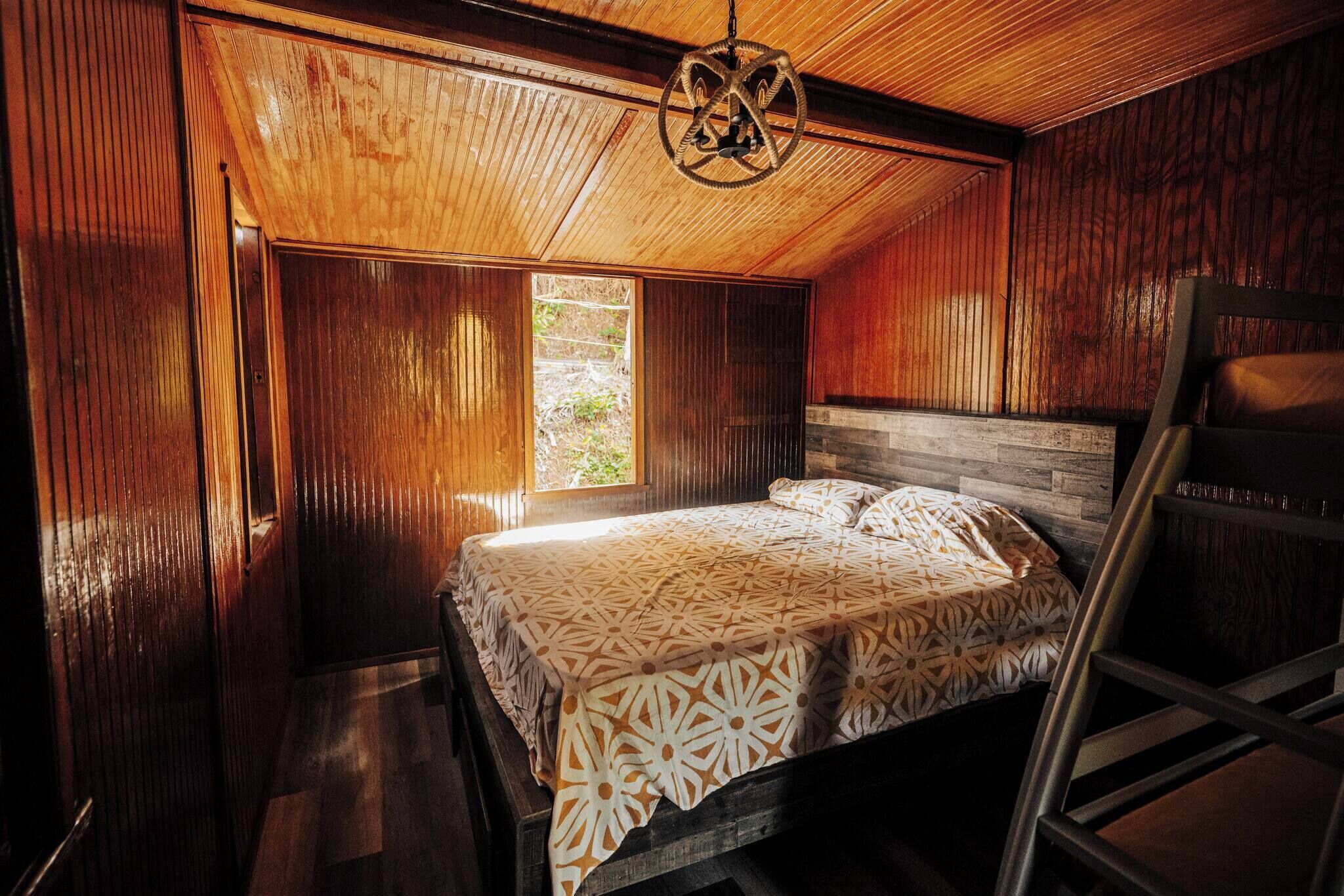 A wooden room with a bed, a window, and a ladder.