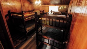 A cabin with wooden walls and floors, bunk beds, a hanging light fixture, and a window. - Naranjito River Retreat | Events & Groups | Sleeps 13 (Naranjito)
