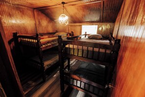 Eine Holzhütte mit Holzwänden und -böden, Etagenbetten, einer Pendelleuchte und einem Fenster.