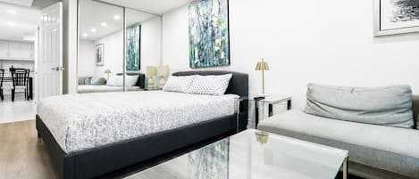 A modern bedroom with a large bed, a sofa, a glass coffee table, and artwork on the walls.