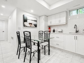 A modern kitchen with white cabinets, a glass dining table, and black chairs. - Spacious and Bright 3-Bedroom Basement Unit in Thornhill (Markham)