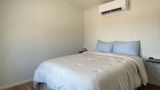 Un dormitorio con cama, mesita de noche, aire acondicionado y luz de techo.