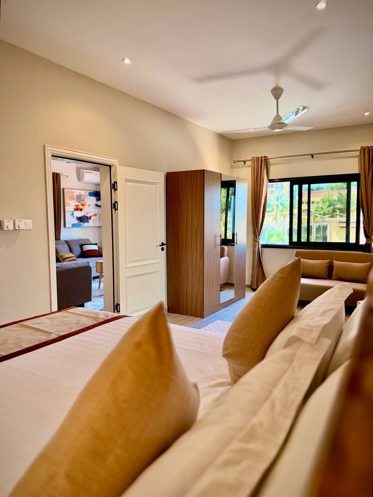 A hotel room with a bed, a ceiling fan, and a view of the outdoors through a window.