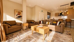 A modern living room with two sofas, a coffee table, and a kitchen area with bar stools. - Teranga Tides (Bijilo)