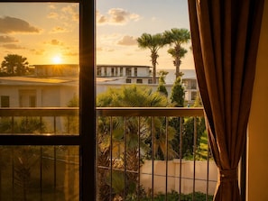 A balcony with a view of a building and palm trees, a railing, and a curtain.