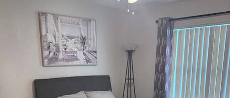 Un dormitorio con cama, escritorio, lámpara de pie y ventilador de techo.