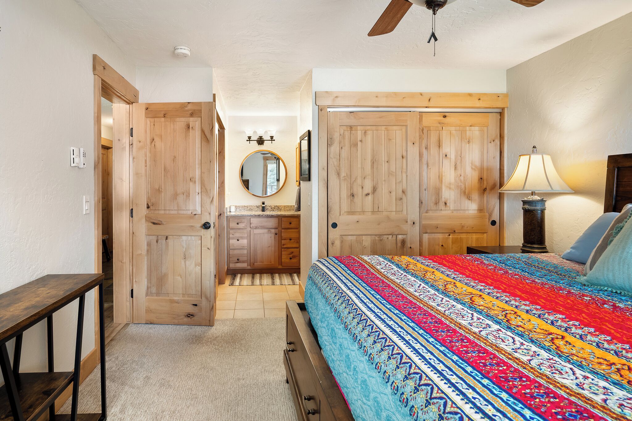 A bedroom with a bed, a nightstand, a lamp, a dresser, a mirror, and a door.