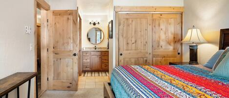 A bedroom with a bed, a nightstand, a lamp, a dresser, a mirror, and a door.