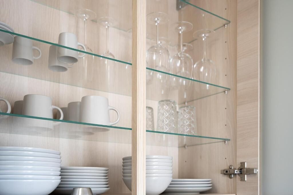 Una cocina con repisas de vidrio que sostienen tazas blancas, platos y copas de vino.
