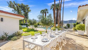 An outdoor dining area with a long table set for multiple guests, surrounded by palm trees and a pool. - Desert Dreams Ranch - Idyllic 6 BR Next to the Polo Grounds (Indio)