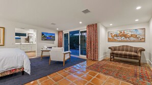 A hotel room with a bed, a desk, a chair, a sofa, a TV, a painting, and a view through the glass door. - Desert Dreams Ranch - Idyllic 6 BR Next to the Polo Grounds (Indio)