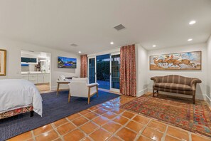 Ein Hotelzimmer mit Bett, Schreibtisch, Stuhl, Sofa, Fernseher, einem Gemälde und Blick durch die Glasdoor.