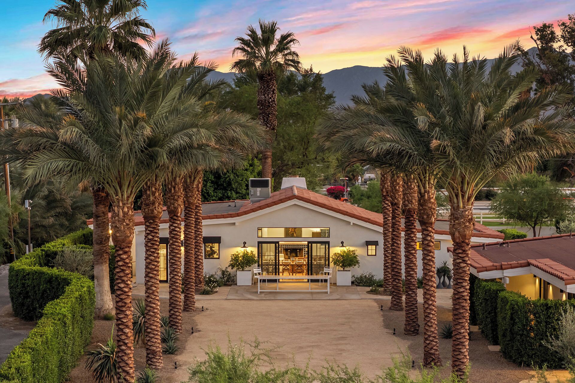 A modern house with a central patio, surrounded by palm trees, and a mountain backdrop.