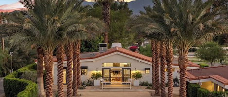 Una casa moderna con un patio central, rodeada de palmeras y montañas al fondo.