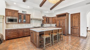Uma cozinha ampla com armários de madeira, uma ilha central com banquetas e piso de ladrilho de pedra.