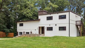 Une maison moderne à deux étages, dotée d’un toit plat, d’un porche à l’avant et d’un escalier menant à un balcon.