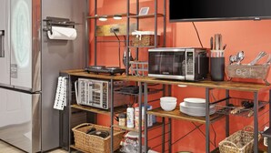 A compact kitchen with a refrigerator, microwave, and a wooden shelf unit with various kitchen items. - Family-Friendly Suite - Springfield METRO (Springfield)