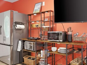 A compact kitchen with a refrigerator, microwave, and a wooden shelf unit with various kitchen items. - Family-Friendly Suite - Springfield METRO (Springfield)