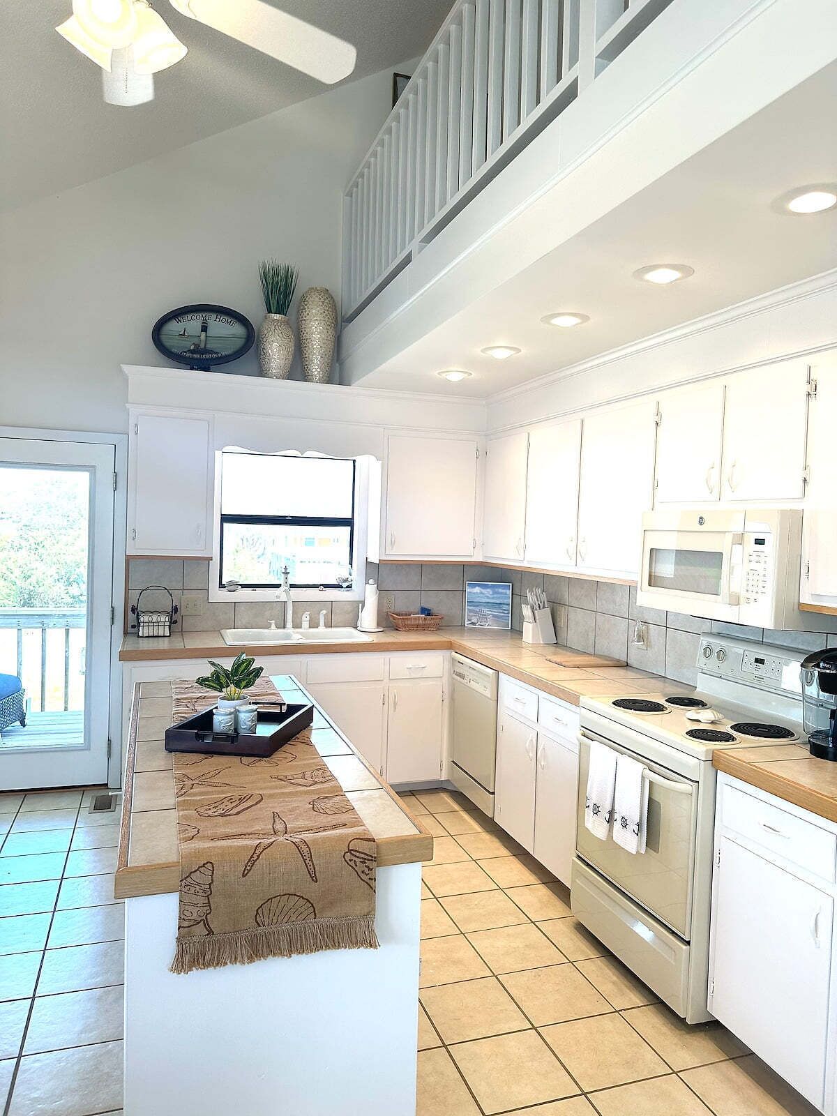 A modern kitchen with white cabinetry, a central island, a microwave, and a stove.