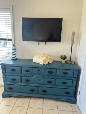 A teal dresser with multiple drawers, a flat-screen TV mounted above it, a small potted plant, and a decorative item resembling a lighthouse.