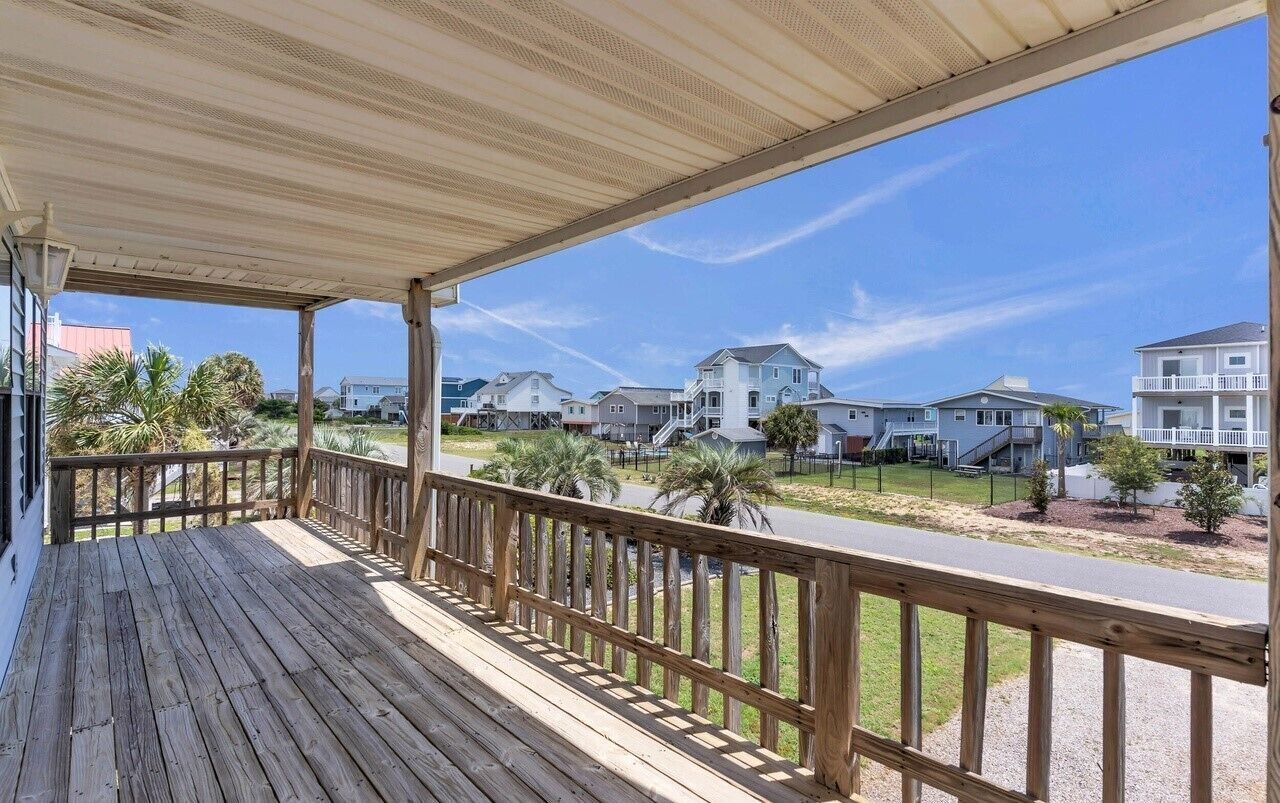 A wooden deck with a railing overlooking a residential street.