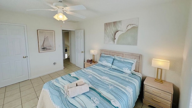 A bedroom with a bed, bedside lamps, a ceiling fan, a door, and a framed picture on the wall.