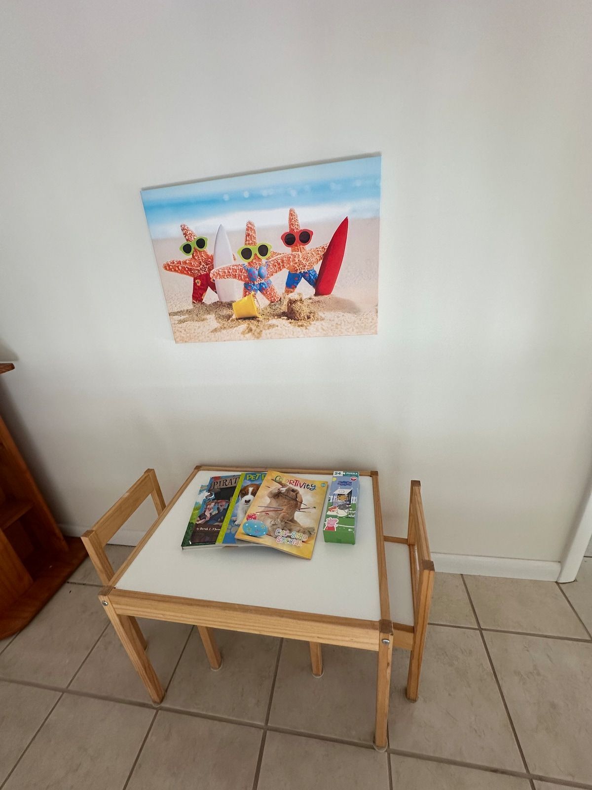 A small wooden table with a magazine and a book on it, placed against a wall with a framed picture above.