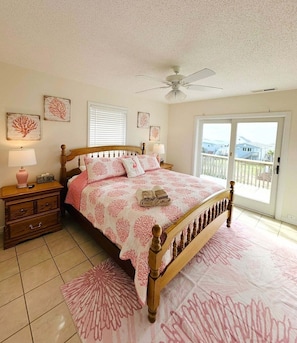 A bedroom with a bed, a nightstand, a lamp, a ceiling fan, and a view through a sliding door.