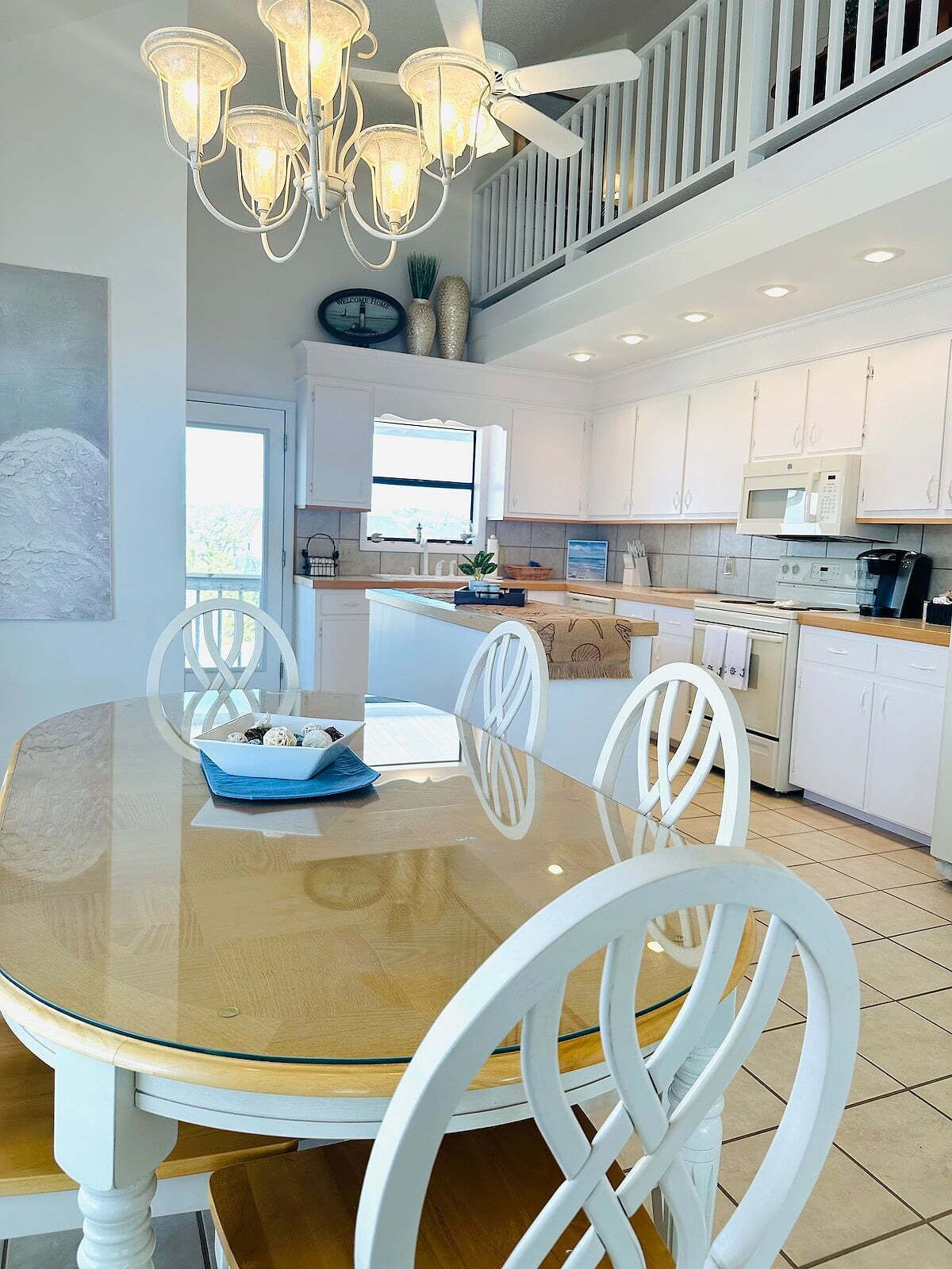 A modern kitchen with white cabinets, a central island, and a dining area with a glass table and white chairs.