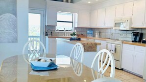 A modern kitchen with white cabinets, a central island, and a dining area with a glass table and white chairs.