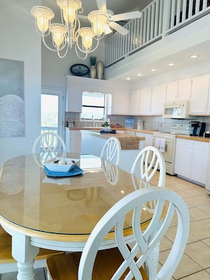 A modern kitchen with white cabinets, a central island, and a dining area with a glass table and white chairs.