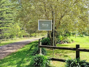 Placa de 'Mera Norfolk Island' com cerca de madeira e vegetação exuberante ao fundo.