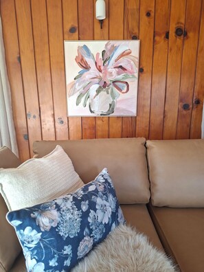 A wooden wall with a painting of flowers, a beige sofa with floral pillows, and a fluffy white rug.