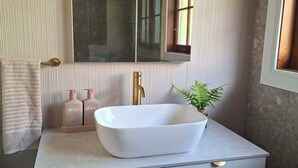 A bathroom with a white vessel sink, a gold faucet, and a mirror above it. - Mera Norfolk Island (Norfolk Island)