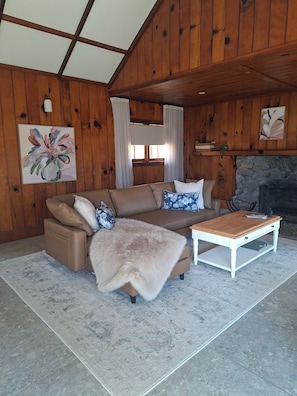 A cozy living room with a brown leather sofa, a white coffee table, and a stone fireplace.