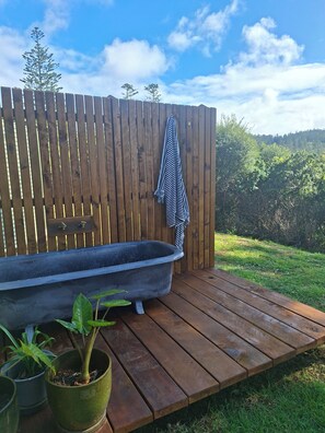A wooden deck with a black bathtub, potted plants, and a wooden fence with a towel hanging on it. - Mera Norfolk Island (Norfolk Island)