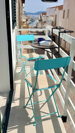 A balcony with turquoise chairs and a table, overlooking a marina with boats and buildings.