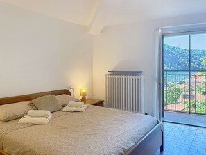 A hotel room with a bed, a nightstand, a lamp, a window with a view of a coastal landscape. - Balconi sulla Spiaggia by Interhome (Bellano)