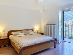 A bedroom with a bed, bedside tables, a lamp, a radiator, and a view of the outside. - Balconi sulla Spiaggia by Interhome (Bellano)